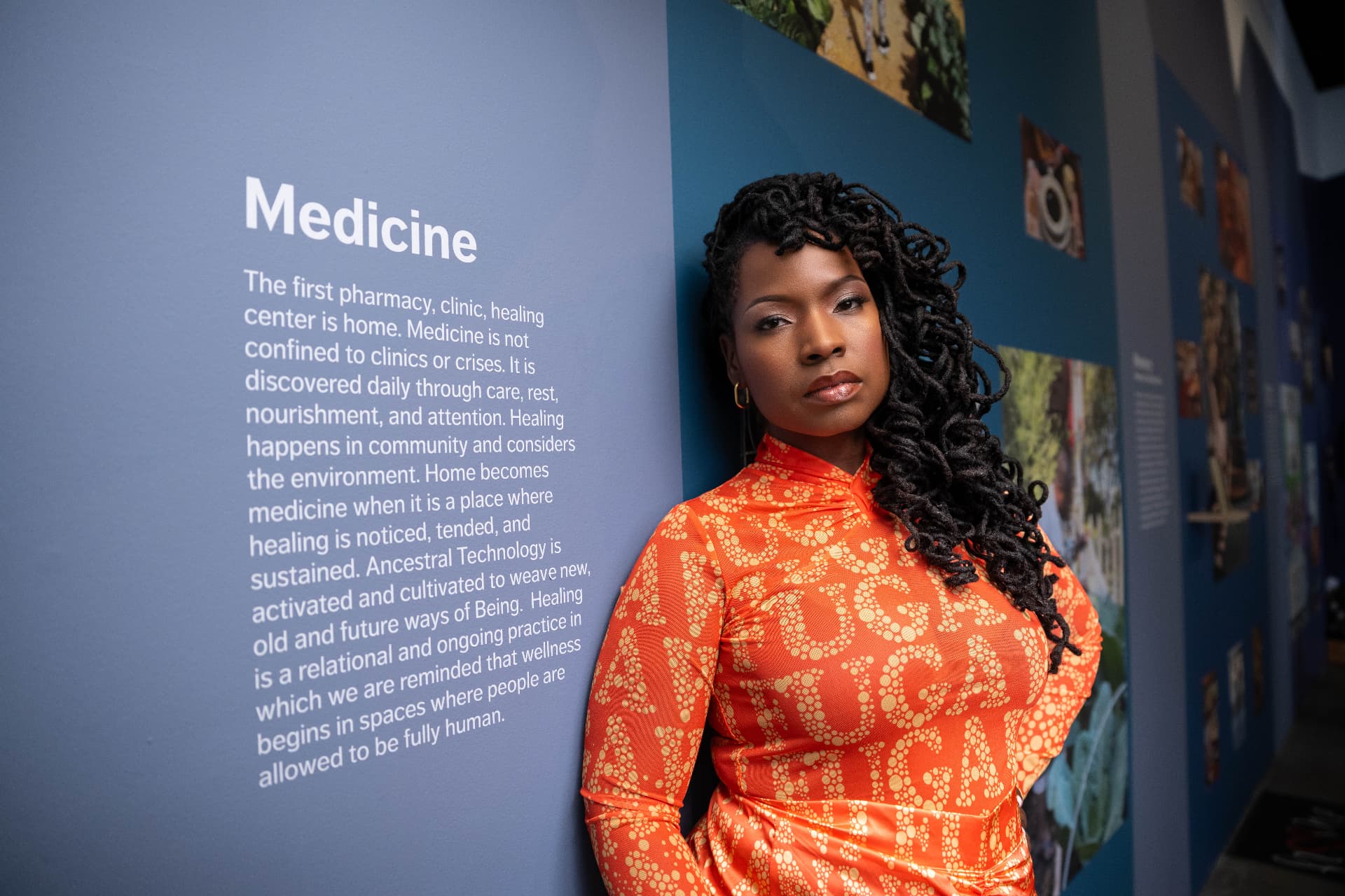 The exhibition's Medicine wall text beside the host in an orange printed dress